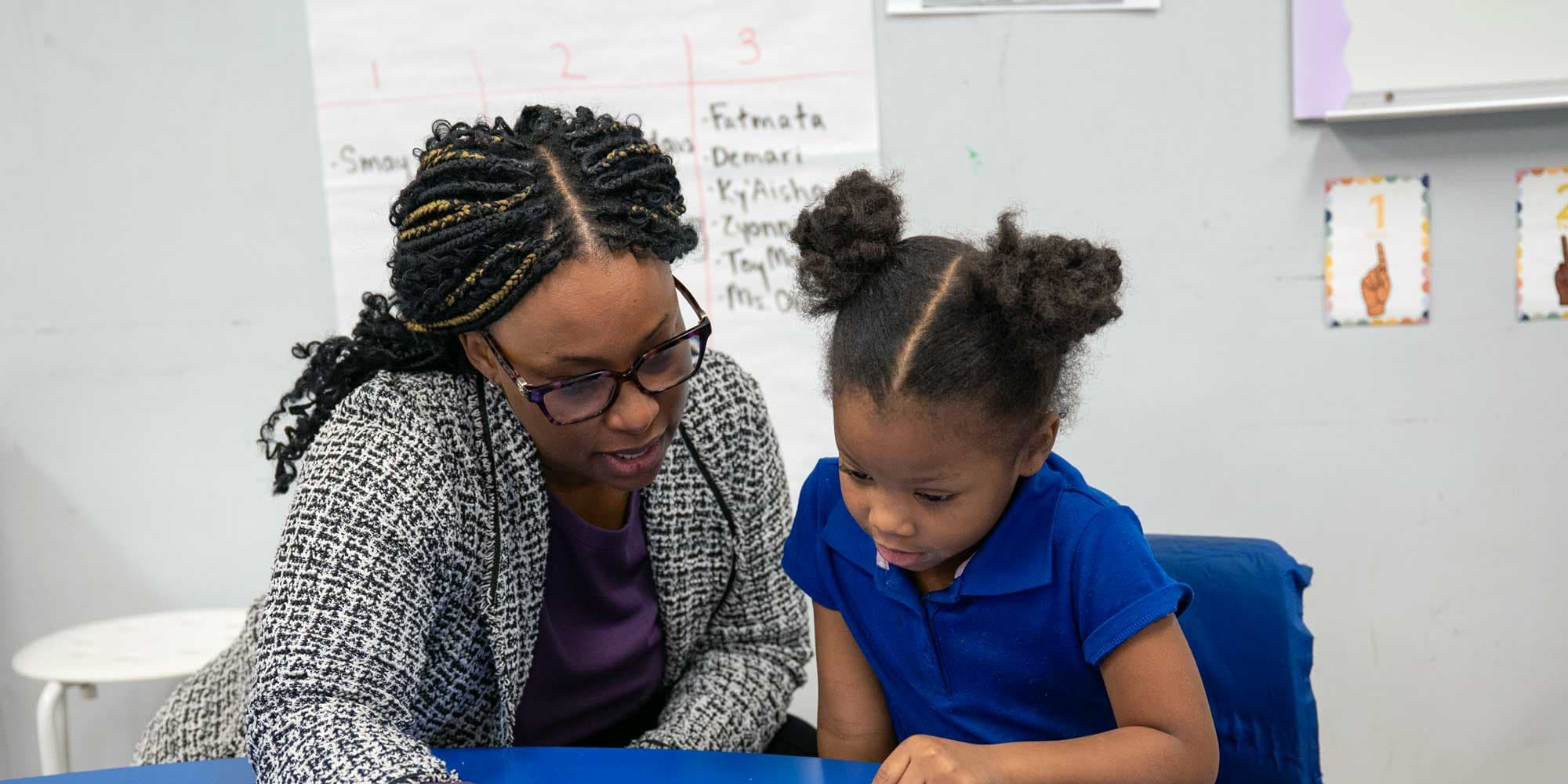 Eastland Prep teacher helping a young student at a classroom table.