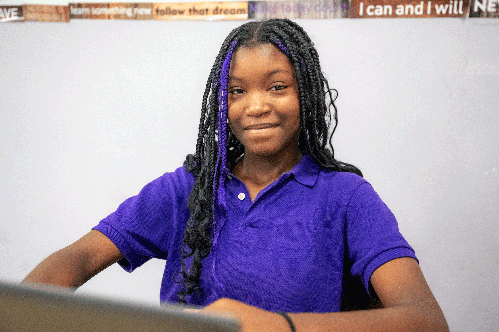 Smiling student in a purple school polo sitting in a classroom.