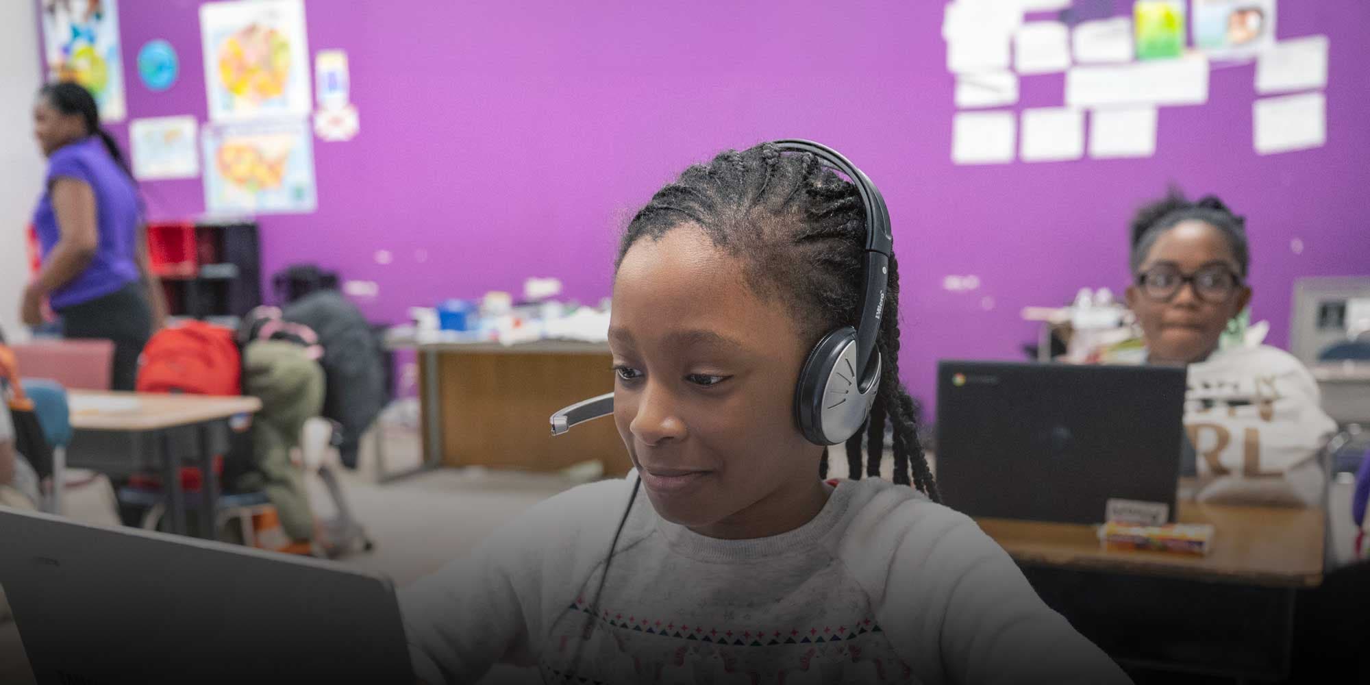 Student wearing a headset works on a laptop in a classroom.