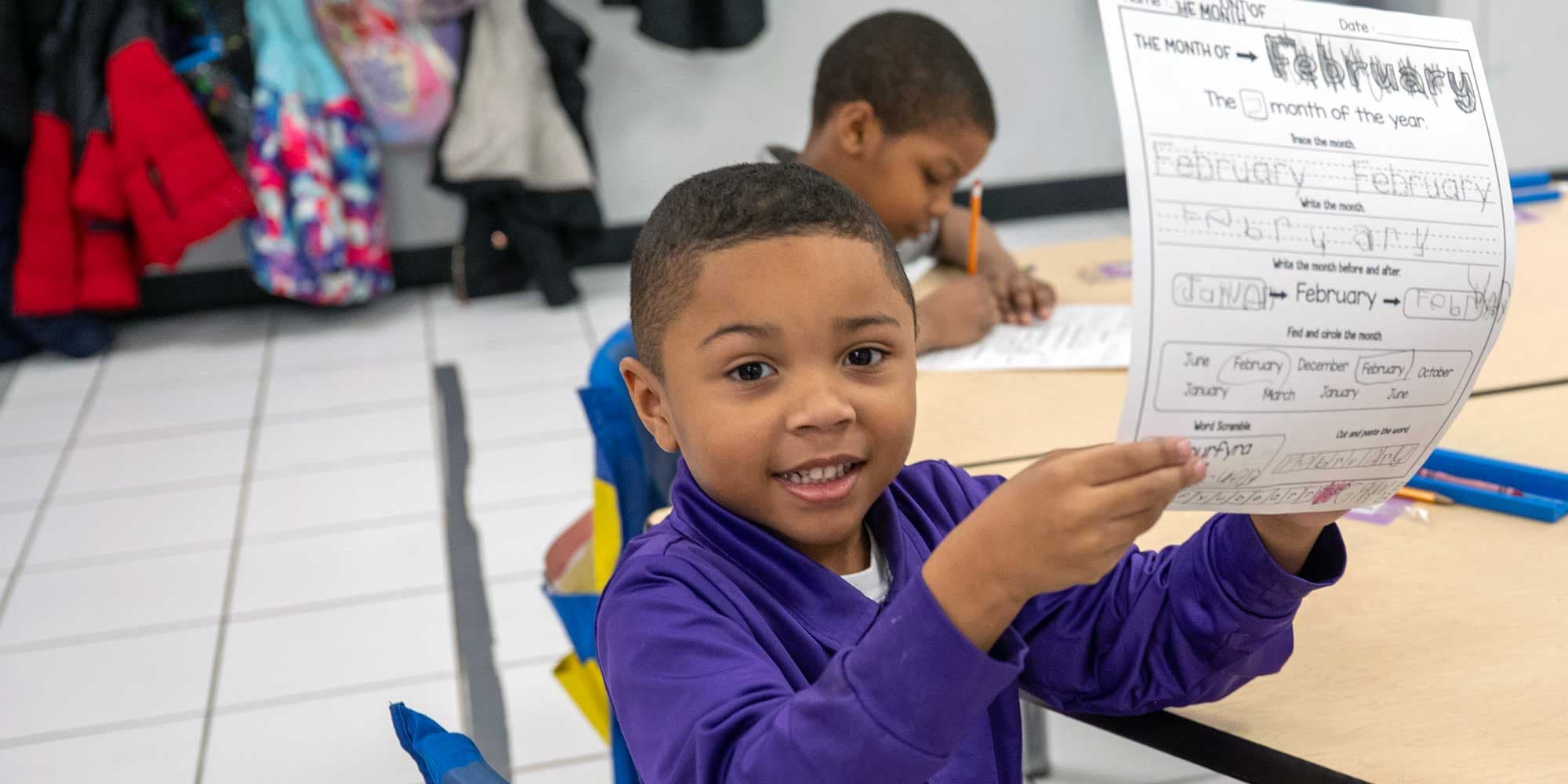 Smiling student holding up a completed worksheet about the month of February.