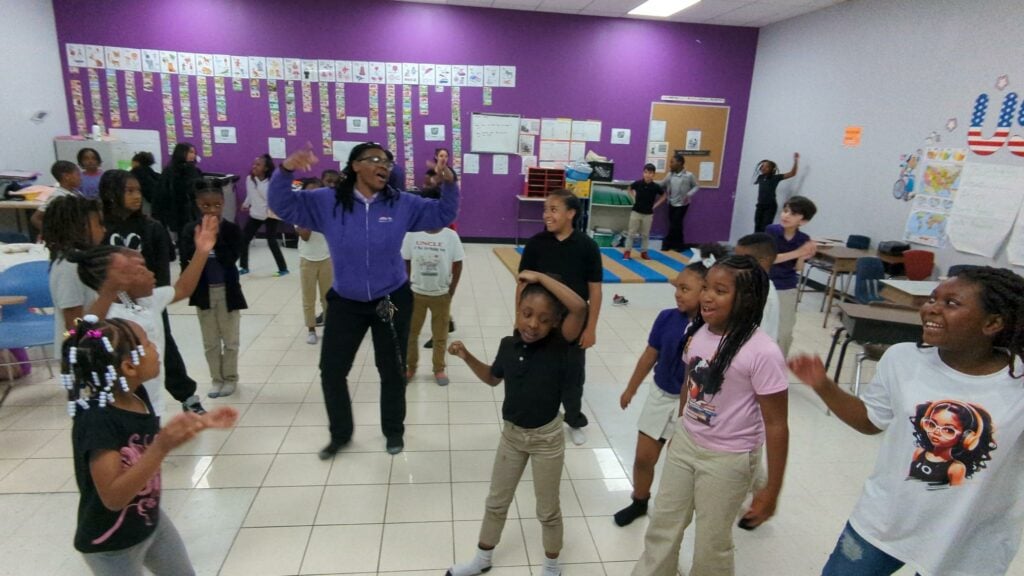 Adult and children dancing and smiling in a classroom.