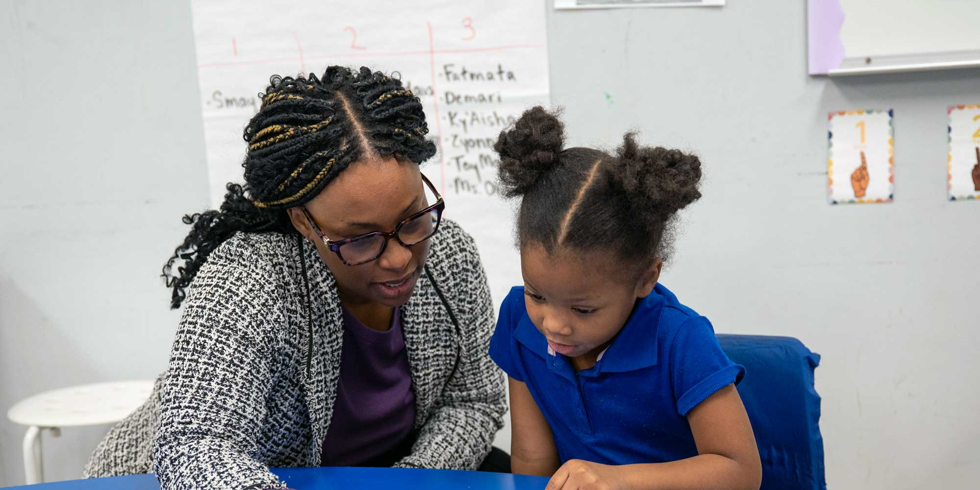Eastland Prep teacher helping a young student at a classroom table.