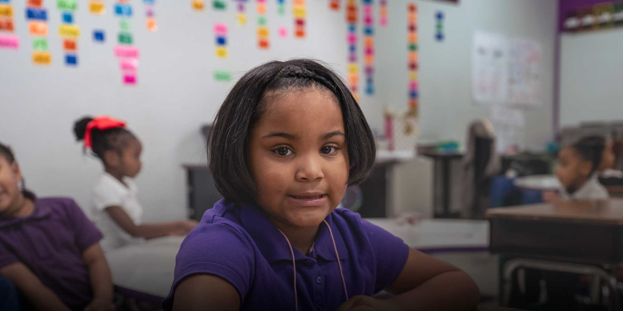 Smiling Eastland Prep student in a purple shirt sitting at a classroom desk.